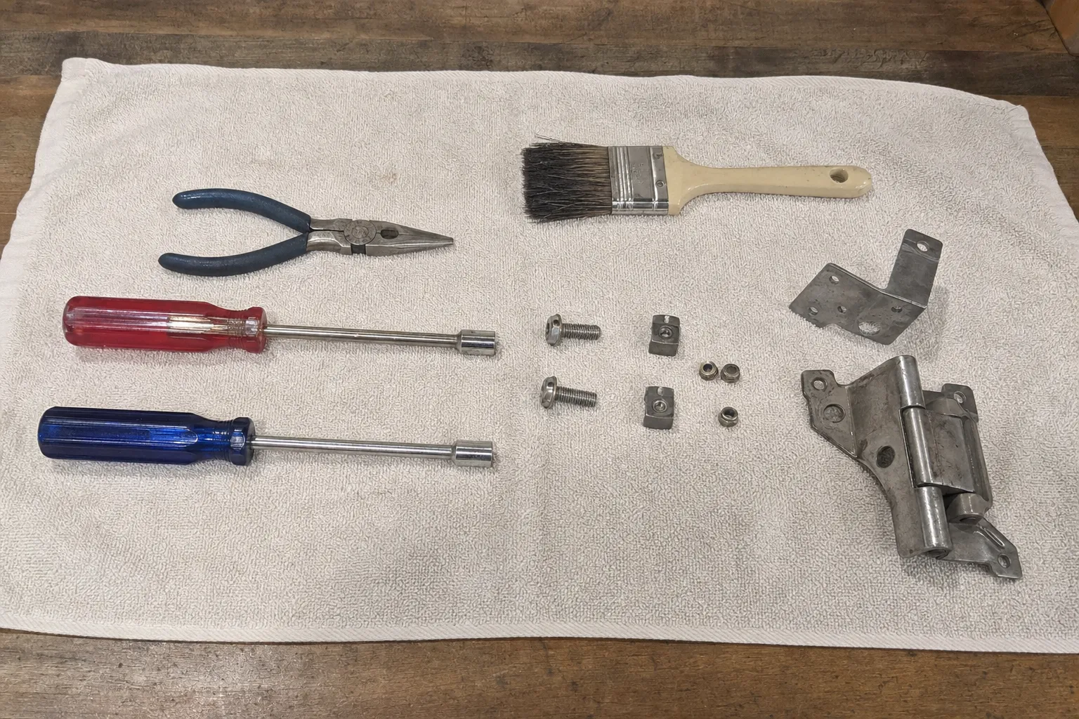 Oven door hinge assembly, fixings and hand tools laid out on a bench cloth before refitting